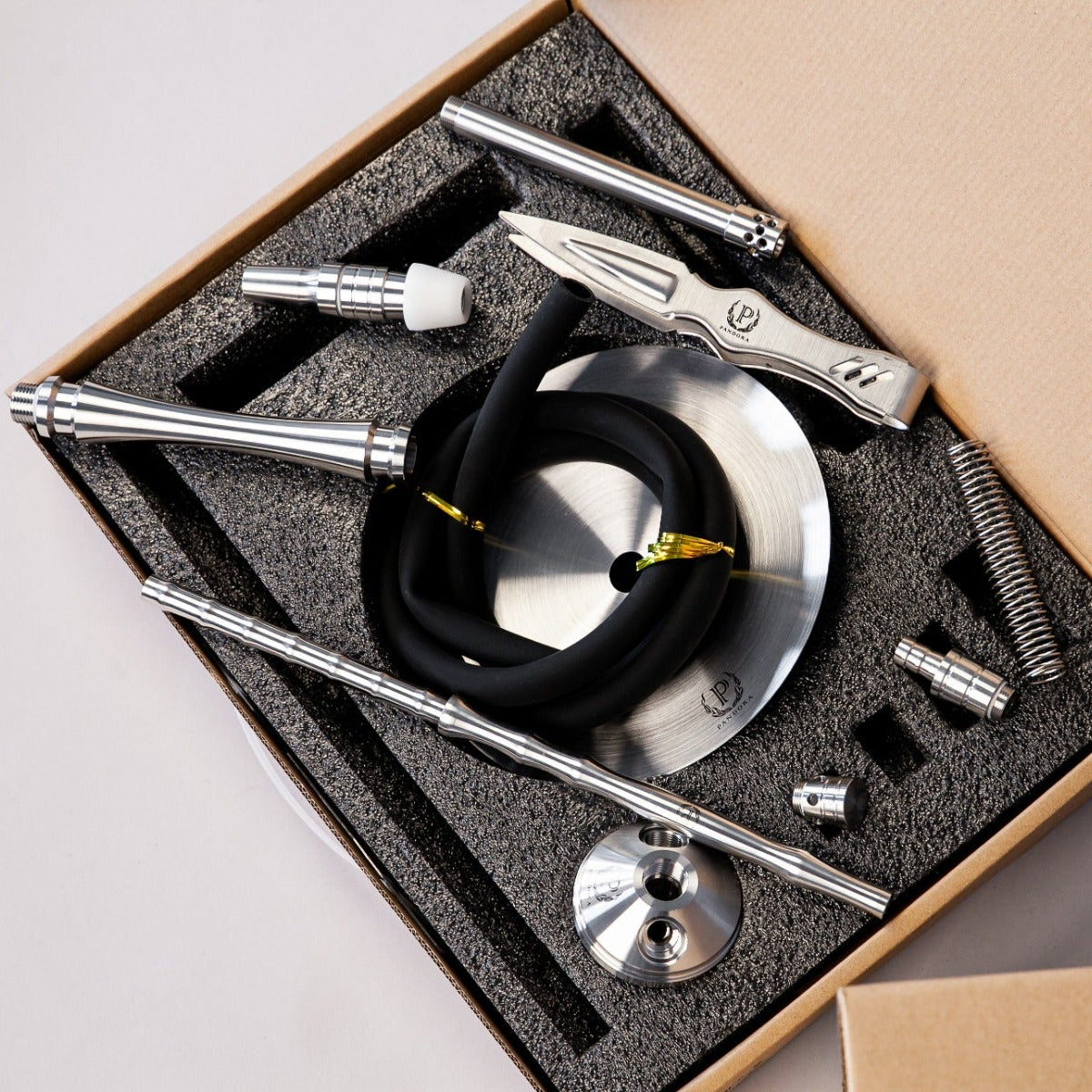 Set of metal tools and components in a cardboard box on a light gray background